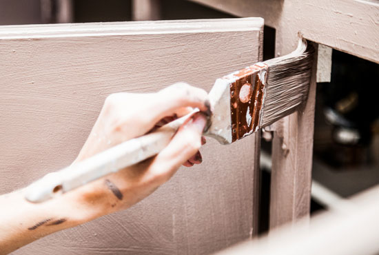 closeup of person painting kitchen cabinets with a brush